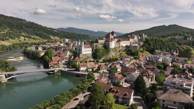 Aerial drone view of Aarburg castle on rock spur above Aare river, old‑town architecture, church spire, flowing water and lush hills in Canton Solothurn, Switzerland.