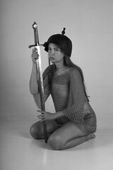 Female warrior in chainmail and original ancient helmet sitting on her knees and holding sword...