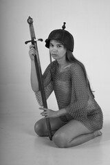Female warrior in chainmail and original ancient helmet sitting on her knees and holding sword...