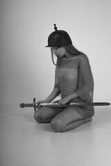Female warrior in chainmail and original ancient helmet sitting on her knees and holding sword...