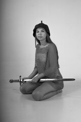 Female warrior in chainmail and original ancient helmet sitting on her knees and holding sword...