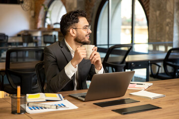 Young caucasian man sitting in the office and having coffee