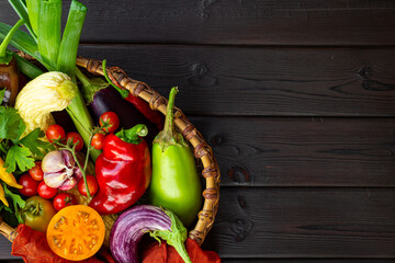 Fresh ripe vegetables in a basket top view, autumn harvest of vegetables on the black wooden...