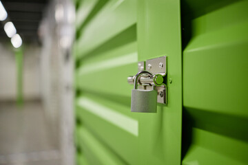Metal padlock securing green storage unit door in indoor facility, focus on lock and latch...