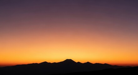 Obraz premium Silhouette of a conical mountain peak against a gradient sunset sky of orange purple and yellow image