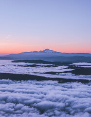 Majestic mountain peak emerges from a sea of clouds at sunrise, with a vibrant purple and orange sky