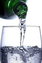 Refreshment with Water Pouring from Green Bottle into Clear Glass on White