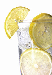Refreshing lemon slices in a glass of sparkling water with ice cubes on white
