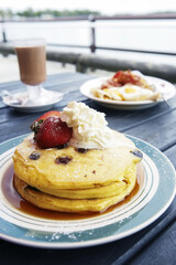 Stack of blueberry pancakes with whipped cream and strawberry on a blue plate
