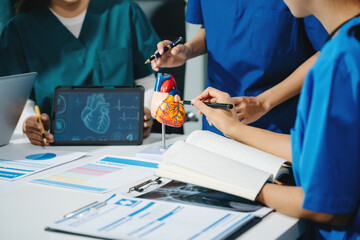 Group of medical students in uniform studying heart anatomy with tablet, notes, and lab reports in...