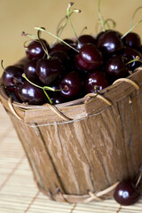 Fresh dark cherries in a wooden basket on a bamboo mat, a healthy snack and summer treat