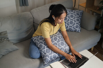 High angle view shot, Young Asian woman sitting on sofa working on laptop in cozy living room at...