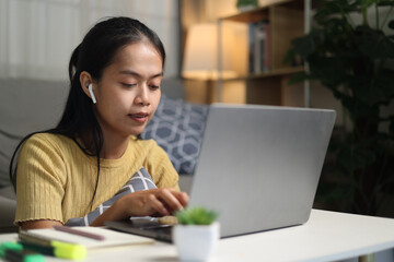 Portrait of Young Asian woman sits on the floor taking online tutoring lessons on a laptop in...