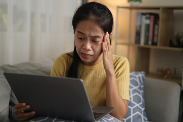 Portrait of Young Asian woman sitting on sofa working on laptop in cozy living room at home. Remote...