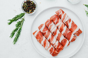 Bacon wrapped sausage rolls on white plate with herbs and oil