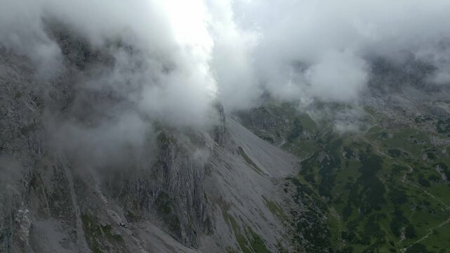 Aerial view of rugged mountains where gray rock meets patches of vibrant green, all partially veiled by ethereal clouds, Muhlbach am Hochkonig, Austria.