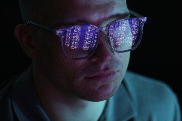Young man wearing glasses with reflection on dark background, closeup