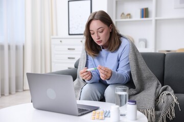 Sick woman with thermometer having online consultation with doctor via laptop at home