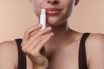 Young woman with lip balm on beige background, closeup