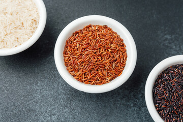 Three types of rice in bowls on dark background top view