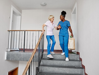 Doctor or nurse caregiver helping disabled senior woman walking down the stairs at home or nursing...