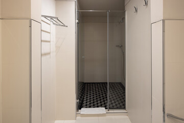 Modern shower room with a glass door, beige tiled walls, geometric black and gray floor tiles