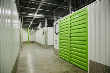 Empty corridor in modern self storage facility showing green metal storage unit doors, concrete...