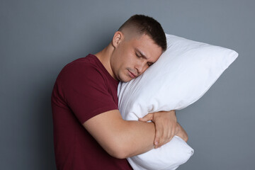 Man with pillow suffering from hangover on grey background