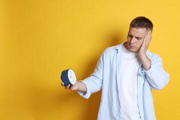 Man with alarm clock suffering from hangover on orange background, space for text