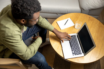 Top view of a young man sitting at the round table and working on laptop