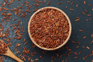 Red rice in wooden bowl with scattered grains and wooden spoon