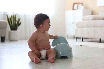 Cute little baby with potty on floor at home