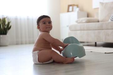 Cute little baby with potty on floor at home