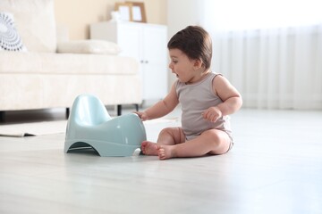 Cute little baby with potty on floor at home