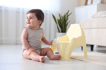 Cute little baby with potty on floor at home