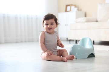 Cute little baby with potty on floor at home