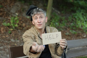 Homeless man with sign Help begging for money on bench in park