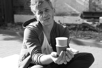Homeless man with paper cups begging for money outdoors. Black and white effect