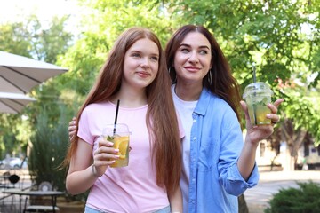 Beautiful mother and her teenage daughter with refreshing drinks outdoors
