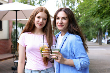 Portrait of beautiful mother and her teenage daughter with refreshing drinks on city street