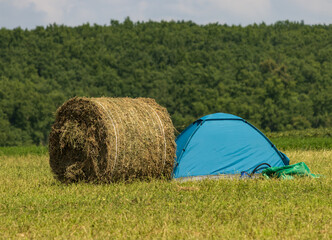 A blue tent is set up in a field next to a hay bale