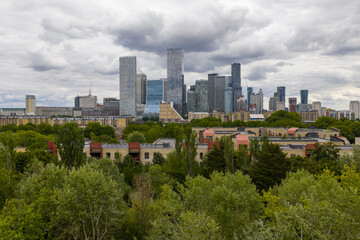 Canary Wharf skyline seen from the west, rising behind trees and low-rise homes.