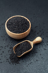 Black sesame seeds in bowl and scoop on dark background