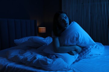 Frustrated woman with pillow suffering from insomnia on bed at home