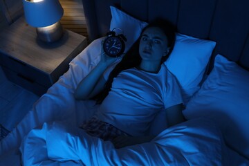 Frustrated woman with alarm clock suffering from insomnia in bed at home, above view