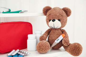 Pediatrics concept. Toy bear with thermometer and pills on white background