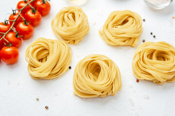 Raw tagliatelle pasta nests with tomatoes and spices on white background