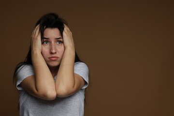 Worried woman suffering from panic attack on brown background, space for text