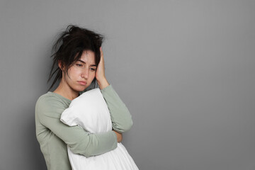 Woman with pillow suffering from hangover on grey background, space for text