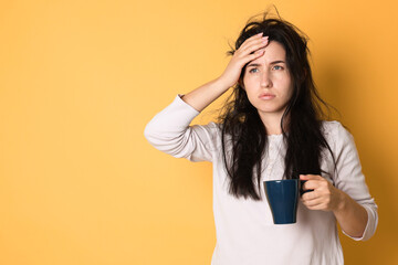 Woman with cup of drink suffering from hangover on orange background, space for text